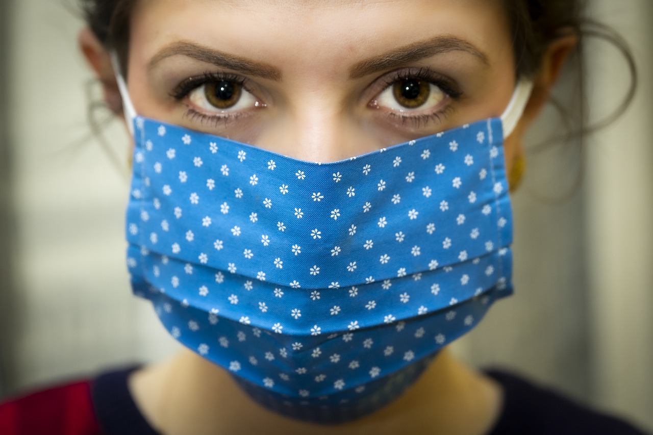 A woman wearing a blue face mask gazes at you unsmiling during the economic recovery.